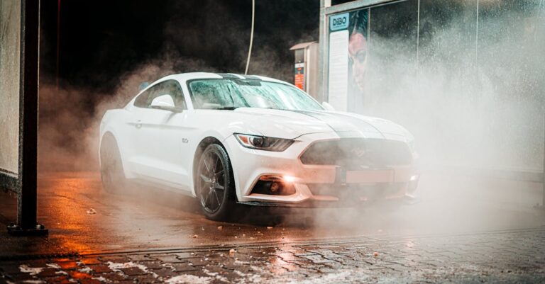 White Ford Mustang in a misty carwash setting, illuminated at night in an urban environment.